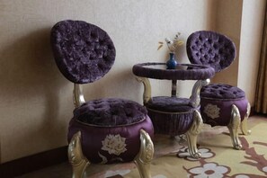 A room with two purple upholstered chairs with gold accents and a small round table with a vase.