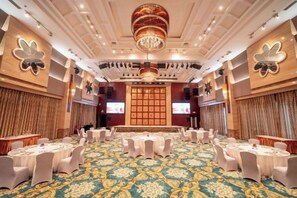 Un salón de banquetes con mesas redondas, una alfombra estampada y una gran lámpara de araña.