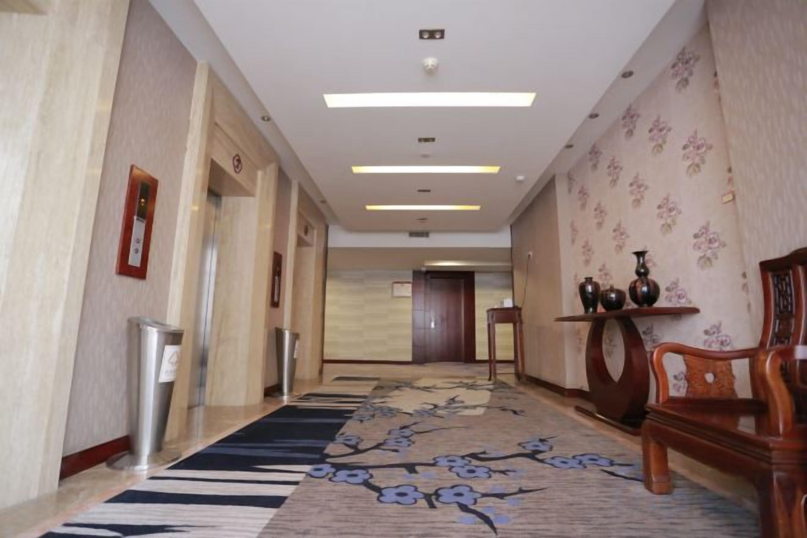 A hotel corridor with a carpet, a reception desk, and a wooden chair.