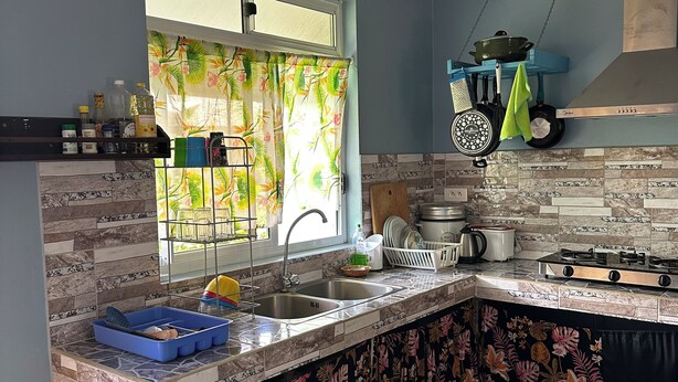 Une cuisine avec une fenêtre, un évier, une cuisinière et un plan de travail sur lequel se trouvent divers objets.