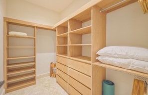 A walk-in closet with multiple wooden shelves and a bed with white bedding. - Modern Lake Villa With English Speaking Staff in Golf and Beach Resort (Punta Cana)