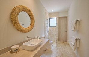 A modern bathroom with a large oval mirror, a rectangular sink, a toilet, and a glass-enclosed shower.