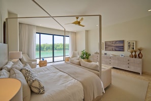 Une chambre moderne avec un grand lit, un ventilateur de plafond, une vue sur l’extérieur, une table de chevet, une commode et une plante.