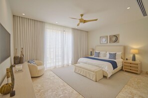 Ein Schlafzimmer mit einem Bett, einem Nachttisch, einem Sessel, einem Deckenventilator und einem großen Fenster mit Vorhängen.