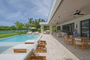 Un espace piscine extérieur moderne, doté de chaises longues, d’un coin salon abrité et offrant une vue sur le paysage environnant.