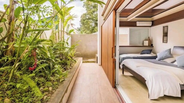 Un dormitorio con dos camas, techo de madera y vistas a un jardín con diversas plantas.