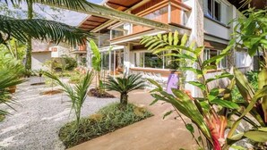 Una casa moderna con un porche cubierto, rodeada de abundante vegetación y un camino de grava.