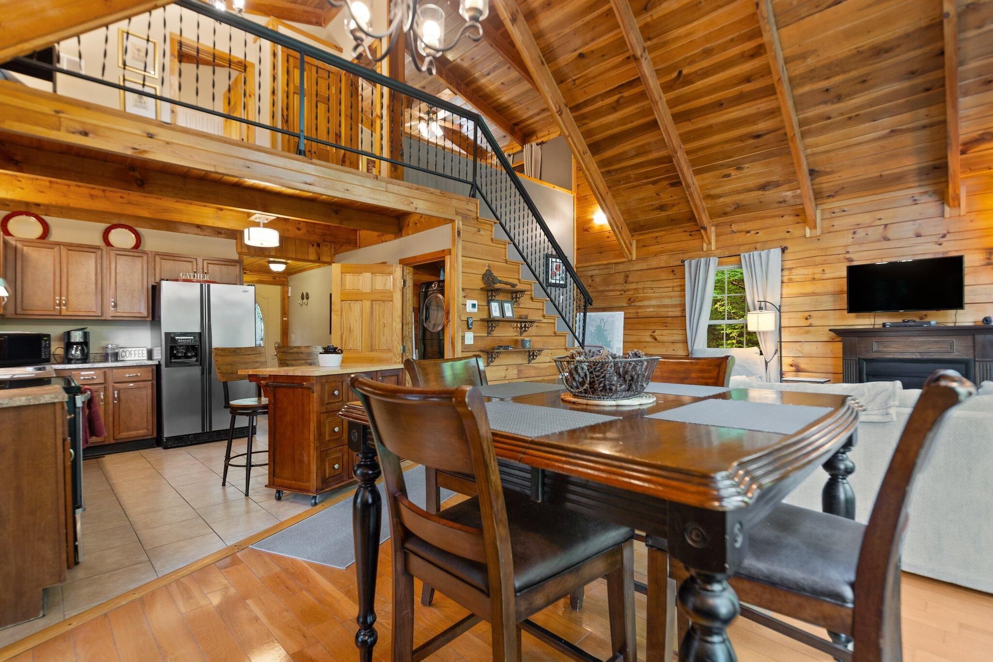 Interior espacioso de una cabaña de madera con cocina, comedor y una escalera que lleva a un altillo.