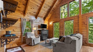 Interior acogedor de una cabaña con paredes de madera, chimenea, sofá y televisor.