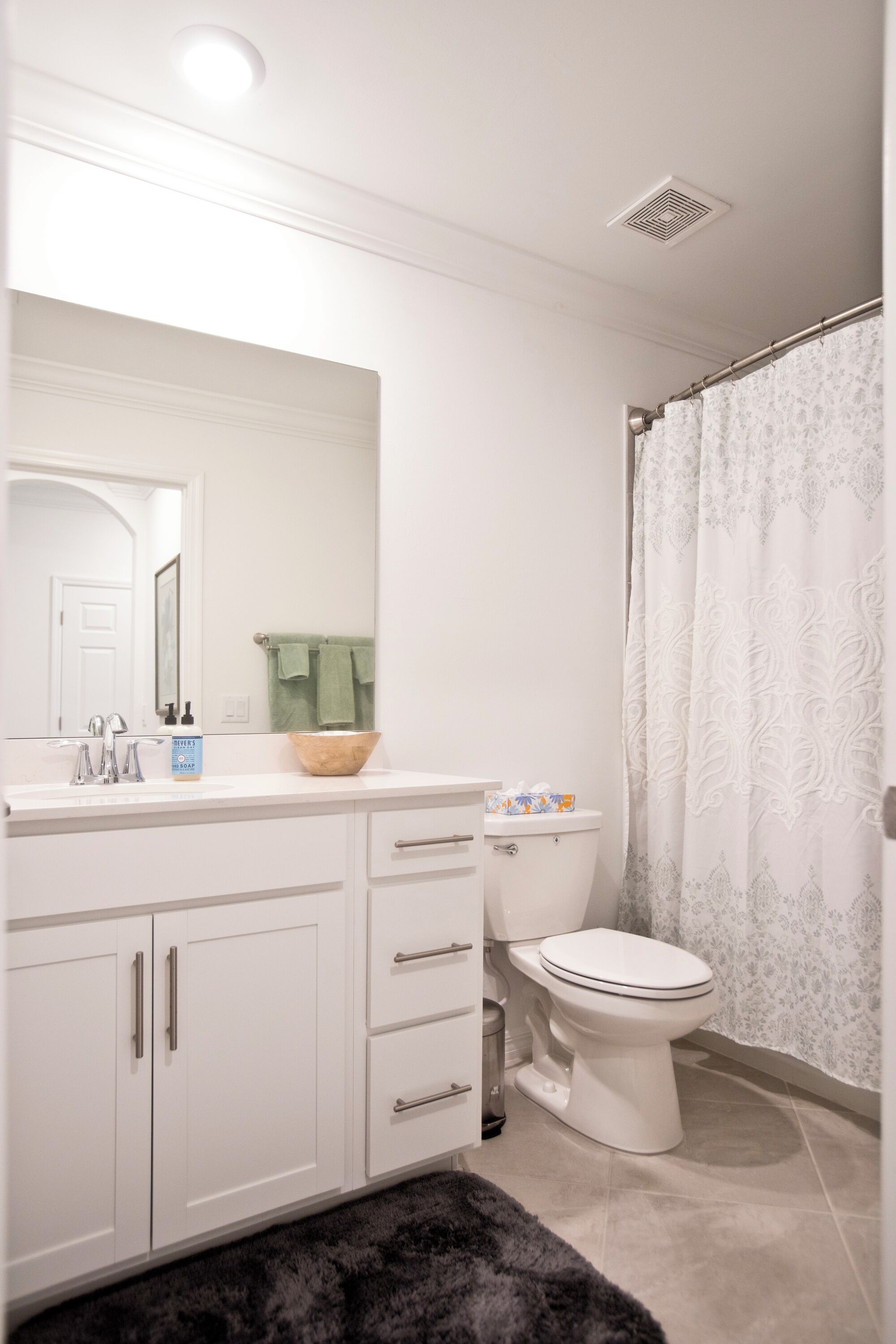 A bathroom with a white vanity, a mirror, a sink, a toilet, and a shower curtain.