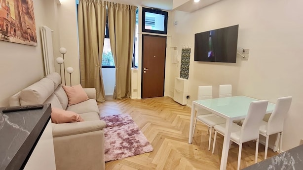 Een moderne woonkamer met een bank, salontafel, eettafel met stoelen, een aan de muur bevestigde televisie en een raam met gordijnen.