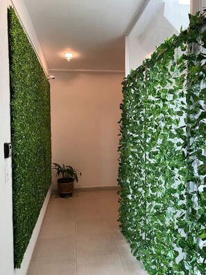 A hallway with green vertical gardens on the walls, a potted plant, and a light fixture on the ceiling.