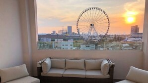 Een balkon met een rieten bank, twee fauteuils, een kleine tafel en een stadsgezicht, inclusief een reuzenrad.