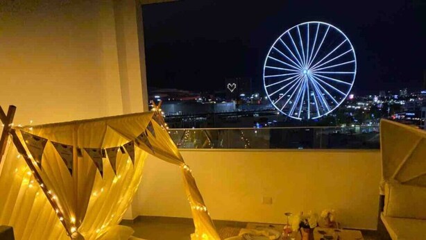 Een balkon met een hemelbed, eettafel en uitzicht over de stad, inclusief een verlichte reuzenrad.