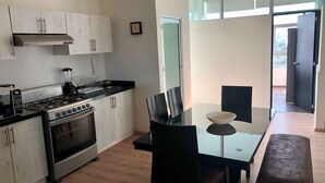 Een moderne keuken met een gasfornuis, oven en witte kasten. Er is een eettafel met stoelen en een bank.
