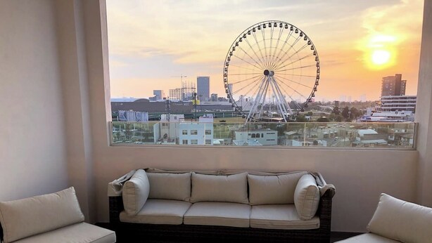 A balcony with a sofa and two chairs, a small table, and a view of a Ferris wheel and cityscape at sunset. - Penthouse in front of Estrella de Puebla 16 guest (Heroica Puebla de Zaragoza)