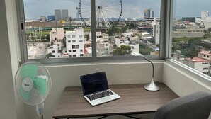 A room with a laptop on a desk, a standing fan, and a view of a cityscape including a Ferris wheel. - Penthouse in front of Estrella de Puebla 16 guest (Heroica Puebla de Zaragoza)