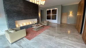 Amplia sala de estar con pared de acento de piedra, una lámpara moderna y un sofá color beige, además de una mesa de centro.