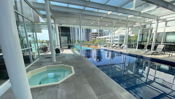 Una piscina interior con paredes de vidrio, un jacuzzi independiente y sillones de descanso.