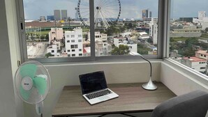 A room with a laptop on a desk, a standing fan, and a view of a cityscape with a Ferris wheel. - NEW Penthouse for 8 in La Estrella de Puebla (Heroica Puebla de Zaragoza)