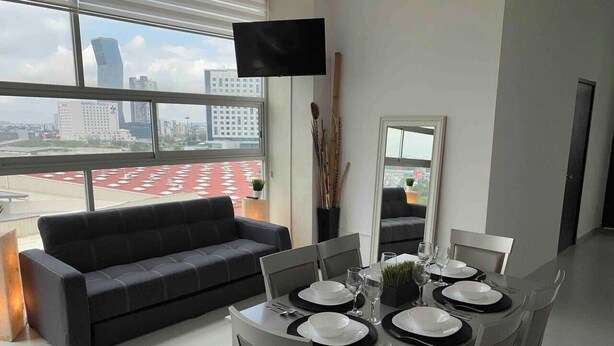 A modern dining area with a round table set for four, a black sofa, and a city view through large windows. - NEW Penthouse for 8 in La Estrella de Puebla (Heroica Puebla de Zaragoza)