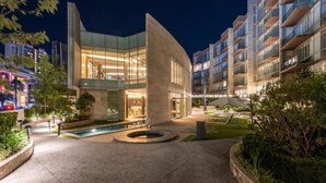 Un hotel moderno con fachada de vidrio curvo, un patio central con piscina y varios balcones.