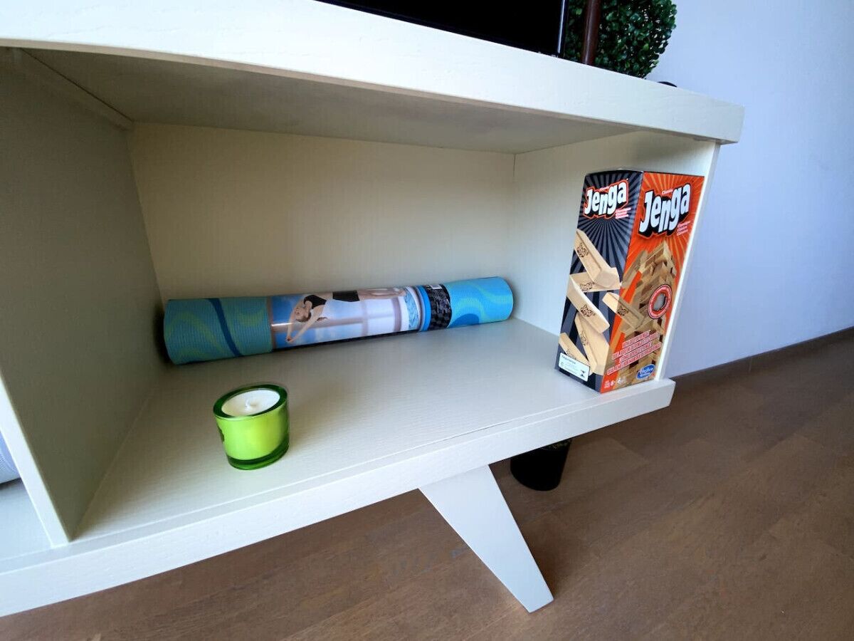 A white shelf with a yoga mat, a candle, and a box of Jenga.