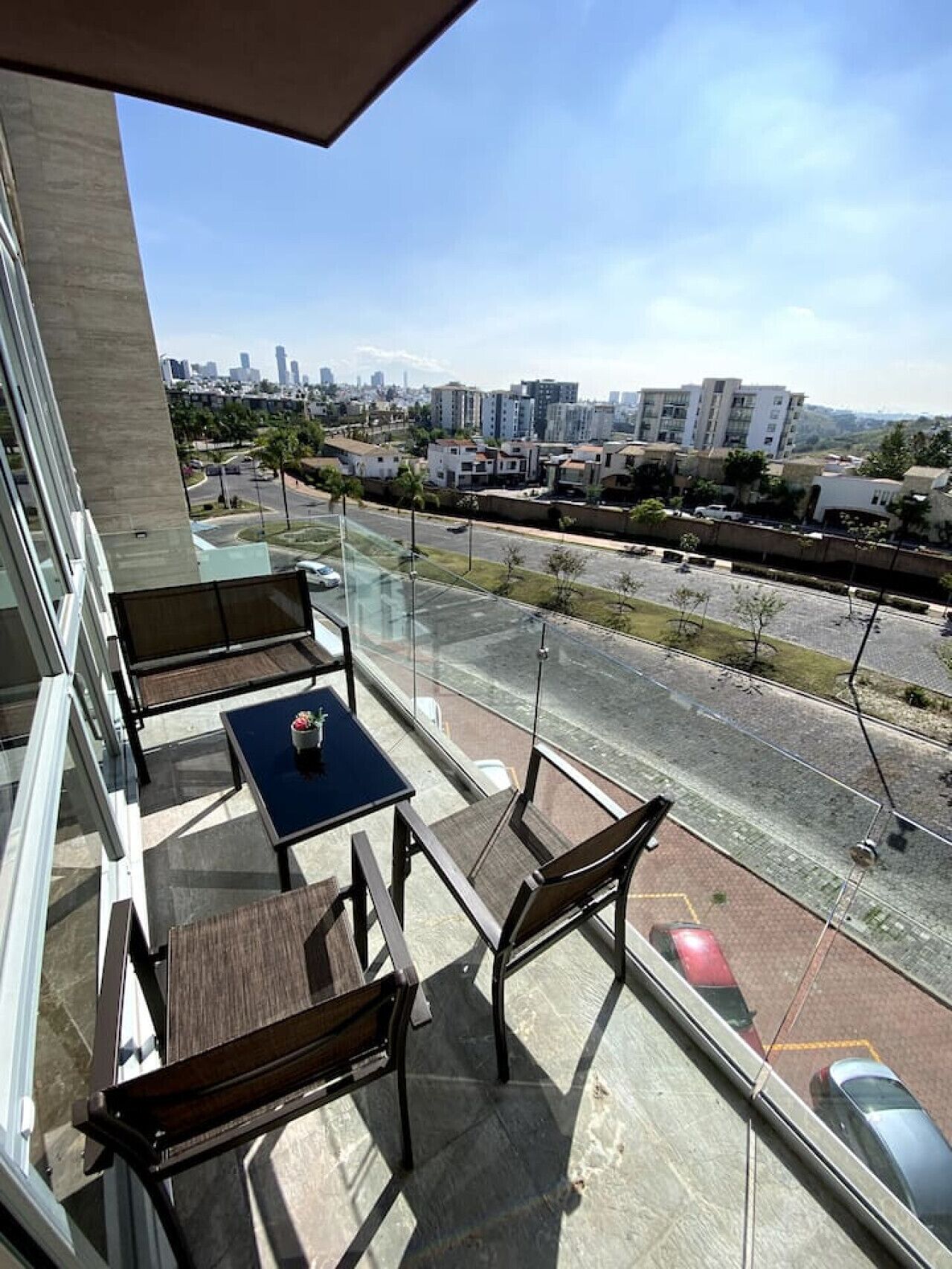 Un balcon avec une table et des chaises, donnant sur un paysage urbain avec des immeubles et une route.