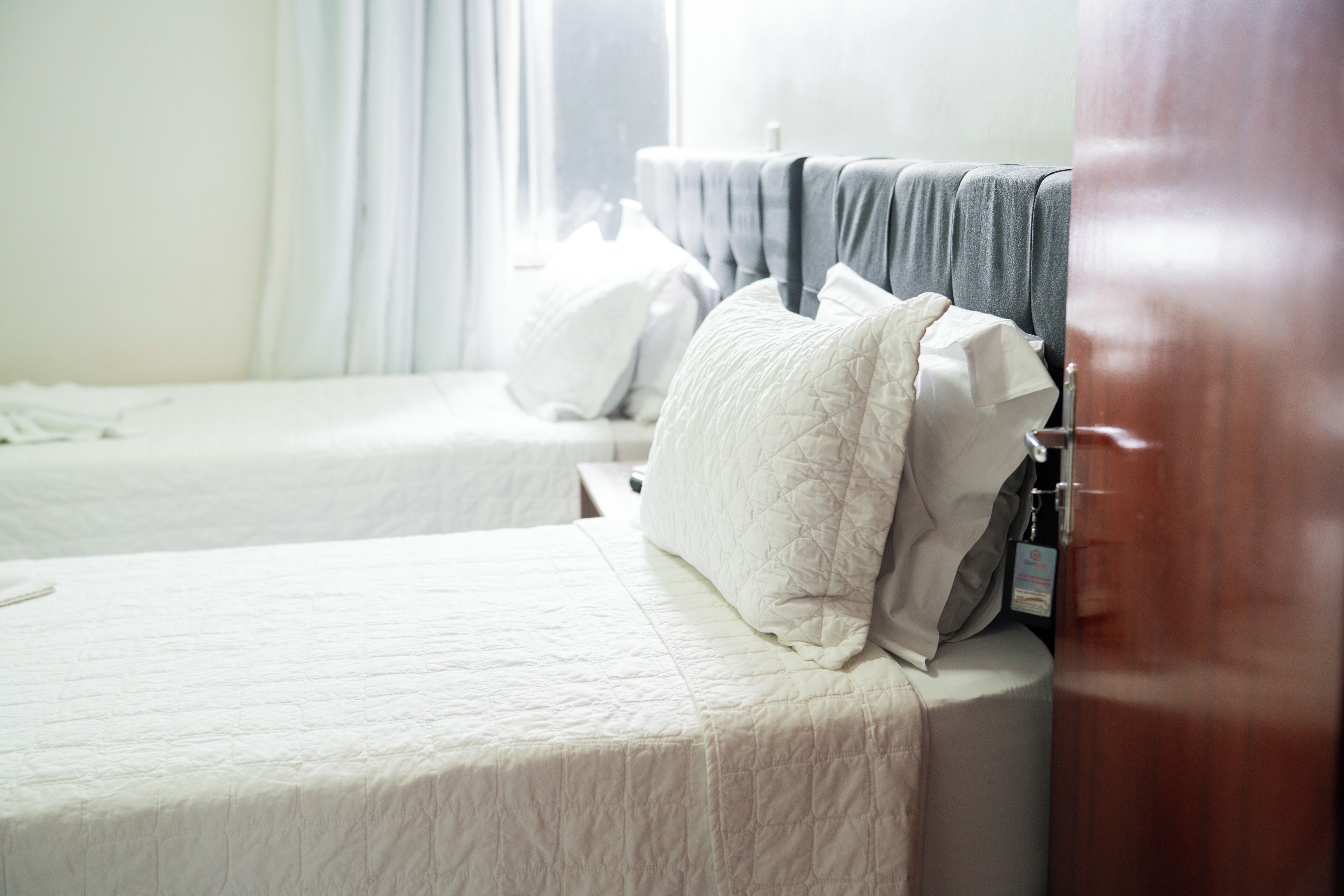 A hotel room with two beds, a wooden door, and a window with curtains.