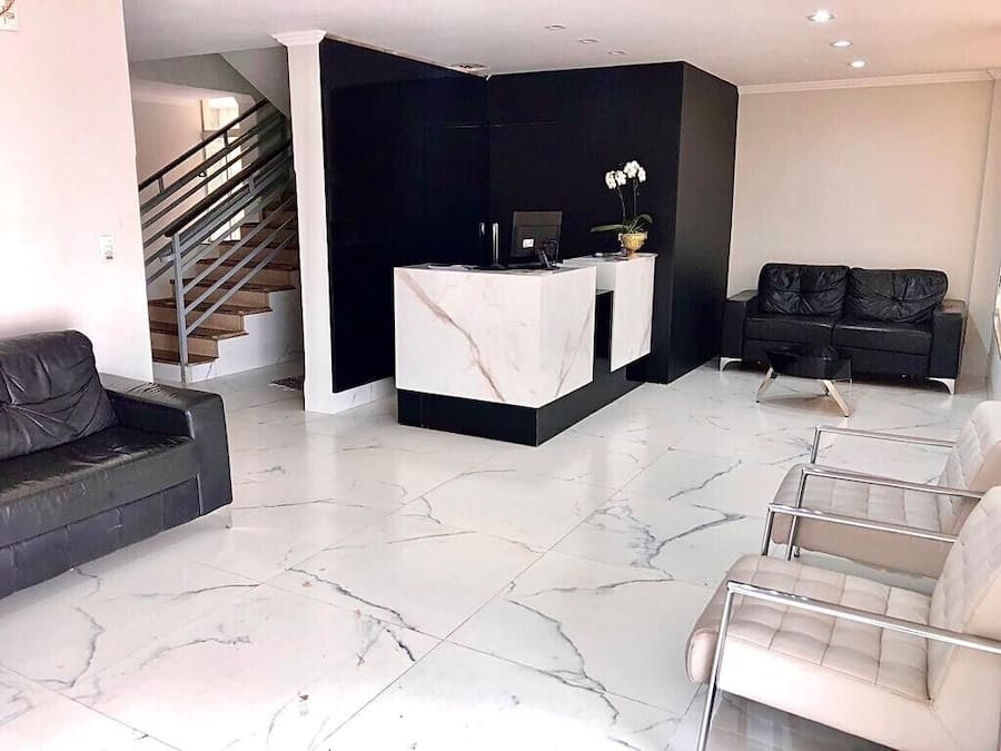 A modern living room with a marble floor, a reception desk, a black sofa, and a staircase.