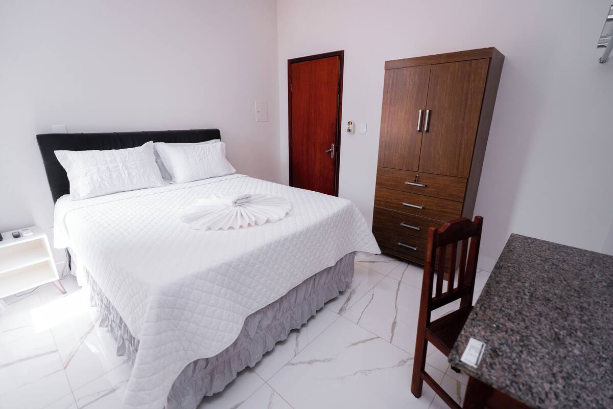 A bedroom with a bed, a wooden wardrobe, a table, and a chair.