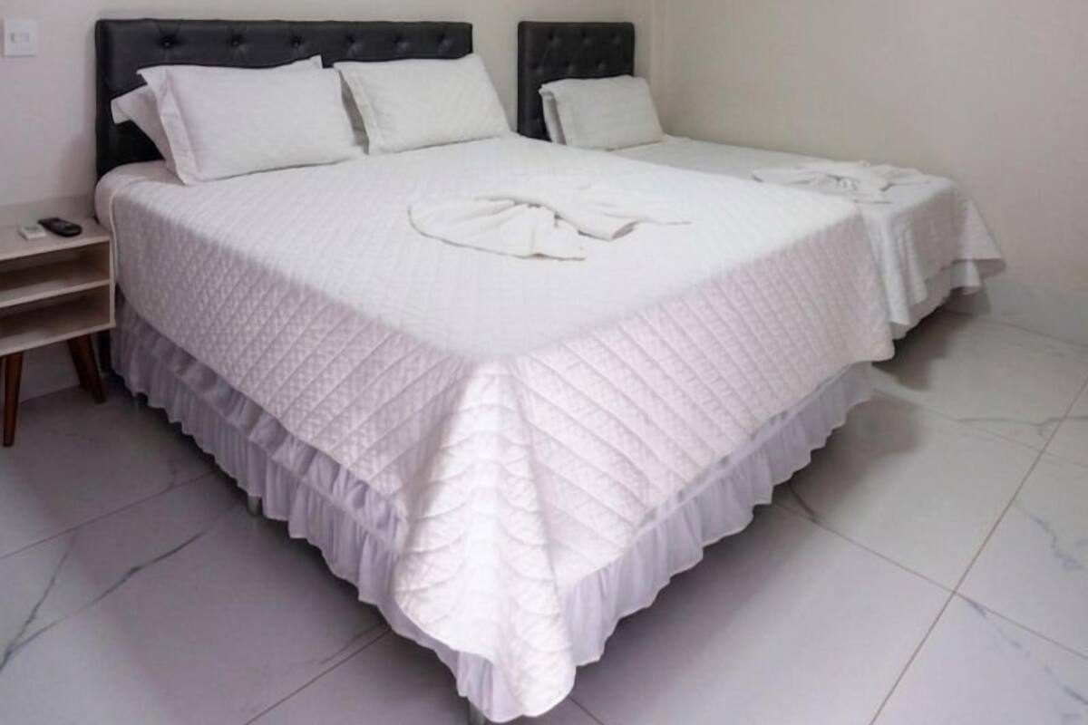 A room with two beds, a nightstand, a wall-mounted air conditioner, and a ceiling light.