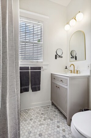 Une salle de bain avec un meuble-lavabo blanc, un robinet doré, un miroir rond et un sol carrelé à motifs hexagonaux.