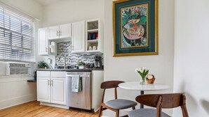 Una cucina compatta con mobili bianchi, un frigorifero in acciaio inossidabile e un angolo ristoro con due sedie e un tavolo.