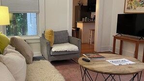 Un salon avec un canapé gris, un tapis moelleux, une table basse ronde et un téléviseur posé sur un meuble en bois.