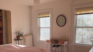 Une chambre à coucher comprenant un lit, un bureau, une chaise, un radiateur et une fenêtre avec des stores.