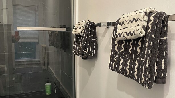 Une salle de bain avec une porte de douche en verre, un porte-serviettes orné de serviettes à motifs et une bouteille verte posée sur le comptoir.