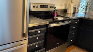 Une cuisine moderne dotée d’appareils électroménagers en acier inoxydable, de meubles de couleur noire et d’un plancher en bois.