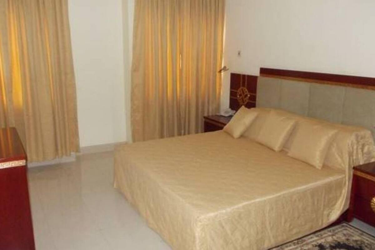 A hotel room with a bed, a nightstand, a lamp, and curtains.
