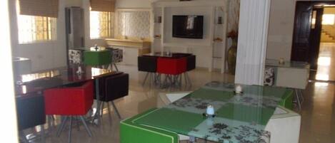 Un soggiorno moderno con un tavolino da caffè in vetro, una TV a schermo piatto montata a parete e un'area pranzo con sedie rosse e nere.