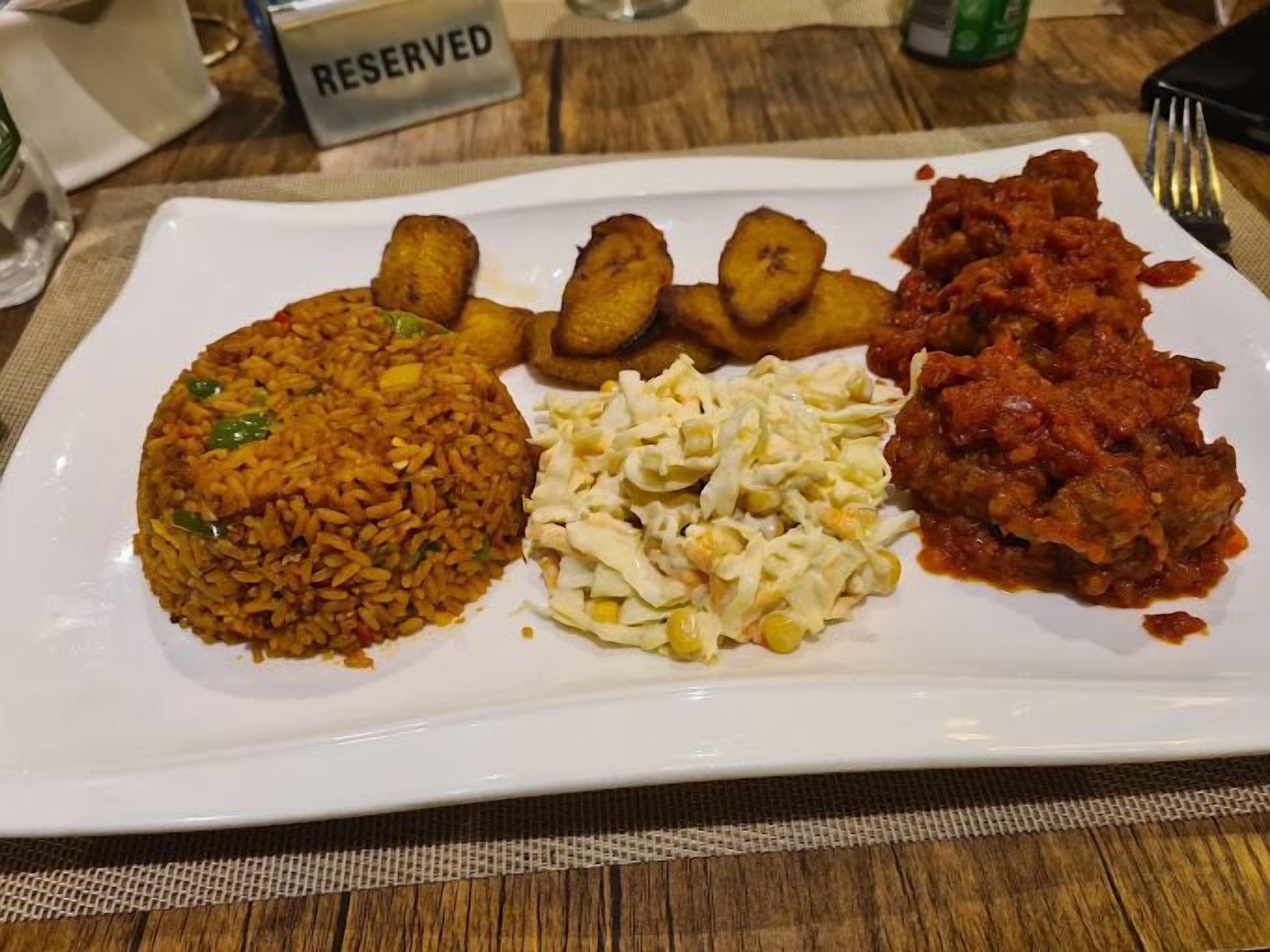 Une assiette de nourriture comprenant du riz, de la salade de chou, des bananes plantains frites et un plat à base de tomates.