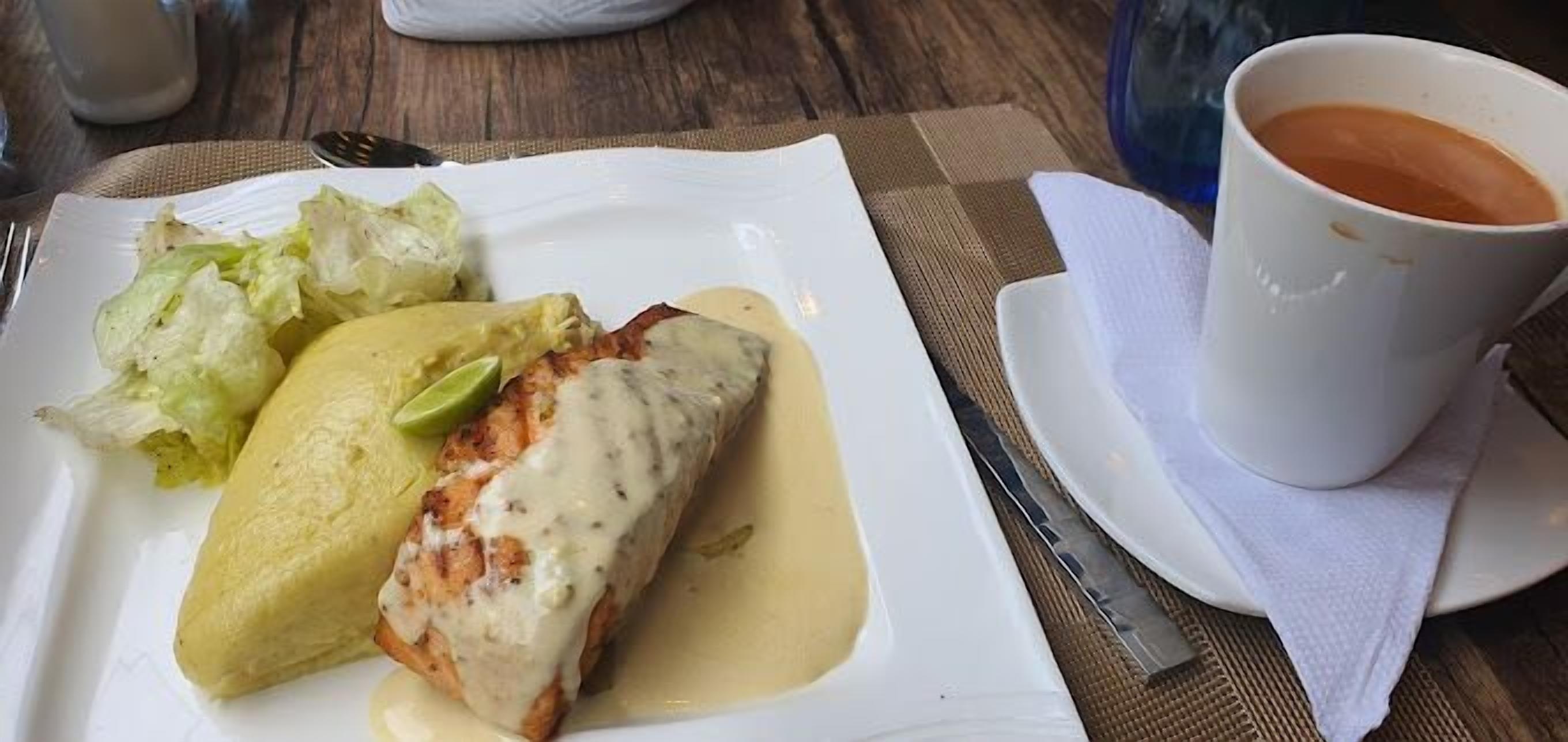 A plate with a fish fillet, a side of lettuce, and a cup of coffee on a table.