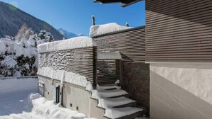 Un edificio moderno con fachada de piedra, listones de madera y techo cubierto de nieve.