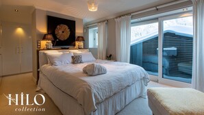 Un dormitorio con una cama grande, dos lámparas de noche, una obra de arte en la pared y vistas a un paisaje nevado a través de amplias ventanas.