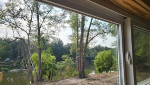 Uitzicht vanuit een raam op een natuurlandschap met bomen en een waterpartij.