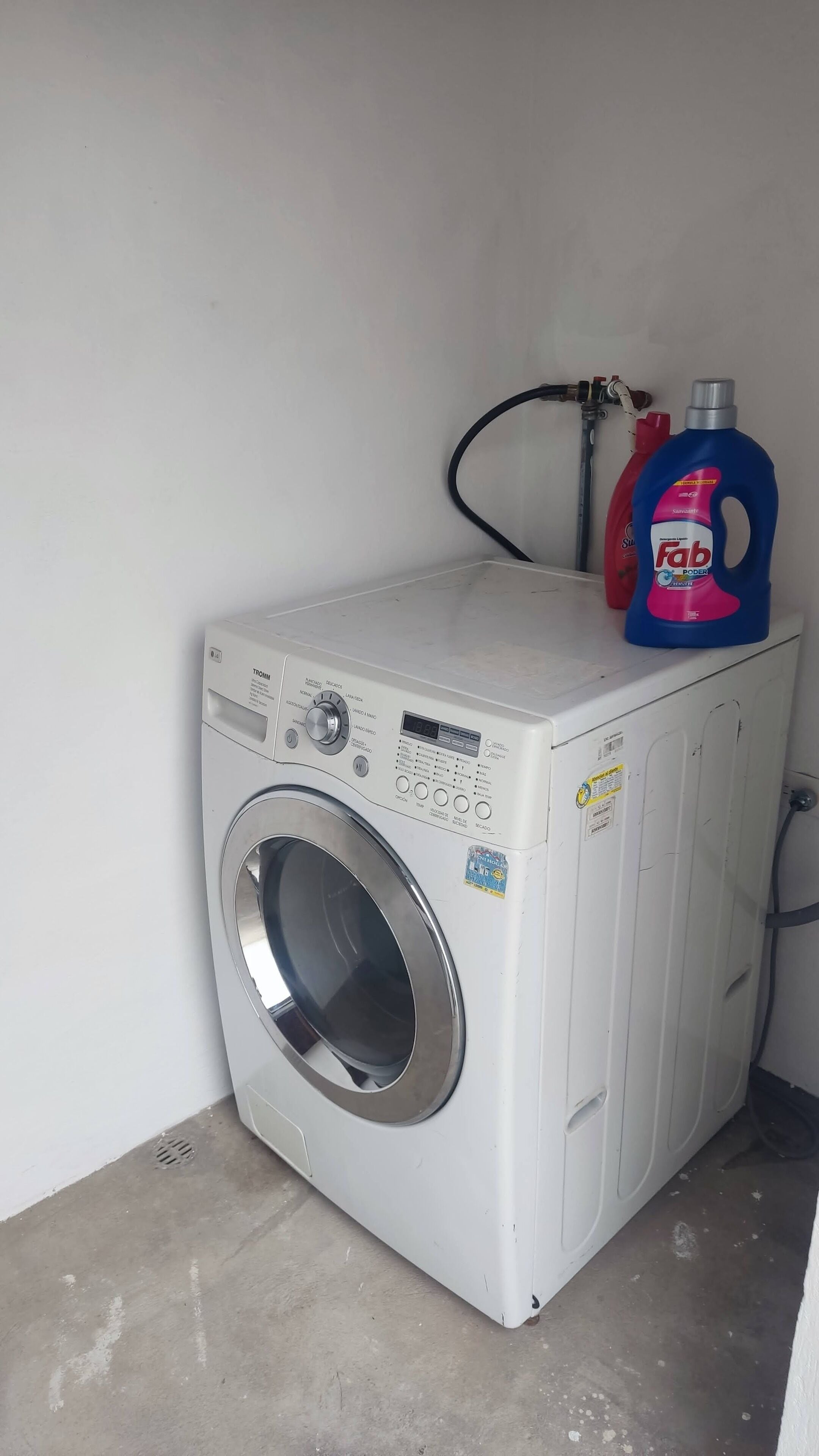 Máquina de lavar com abertura frontal, painel de controle, uma embalagem de detergente e uma mangueira.