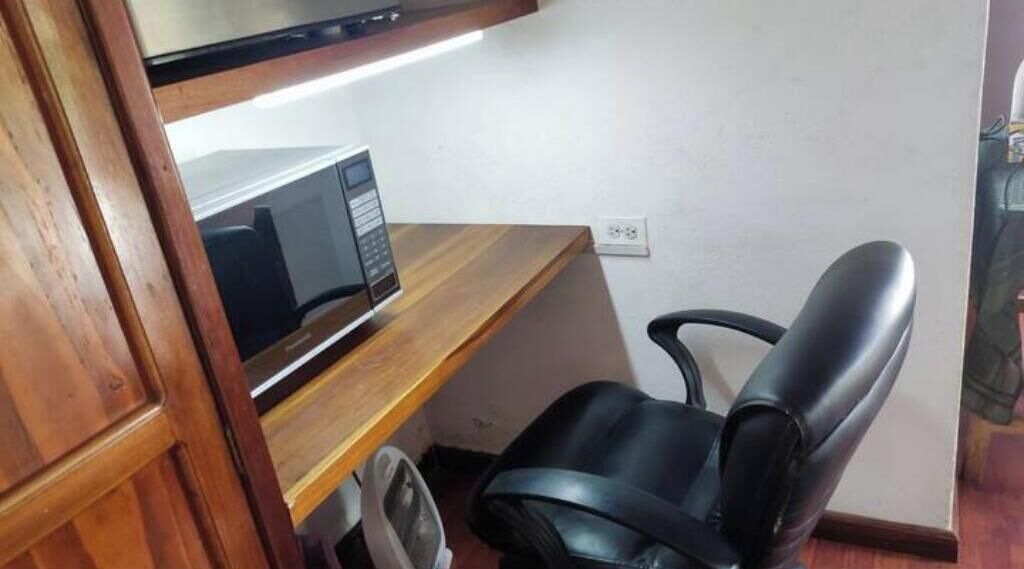 Un petit bureau avec un bureau en bois, une chaise de bureau noire et un four à micro-ondes.