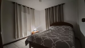 Une chambre à coucher avec un lit, des rideaux, une table de chevet avec une lampe et un luminaire fixé au mur.