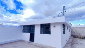 Un bâtiment moderne de couleur blanche, doté de grandes fenêtres et d’une petite porte, entouré d’une zone en béton avec quelques marches menant à l’entrée.