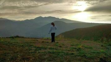 A person standing on a grassy hill with mountains in the background.